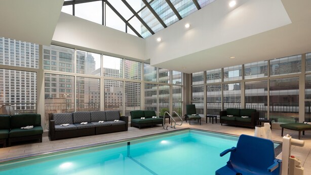 An indoor swimming pool with a glass ceiling, multiple seating areas, and city views. - Hilton Garden Inn Chicago Downtown/Magnificent Mile (Chicago)