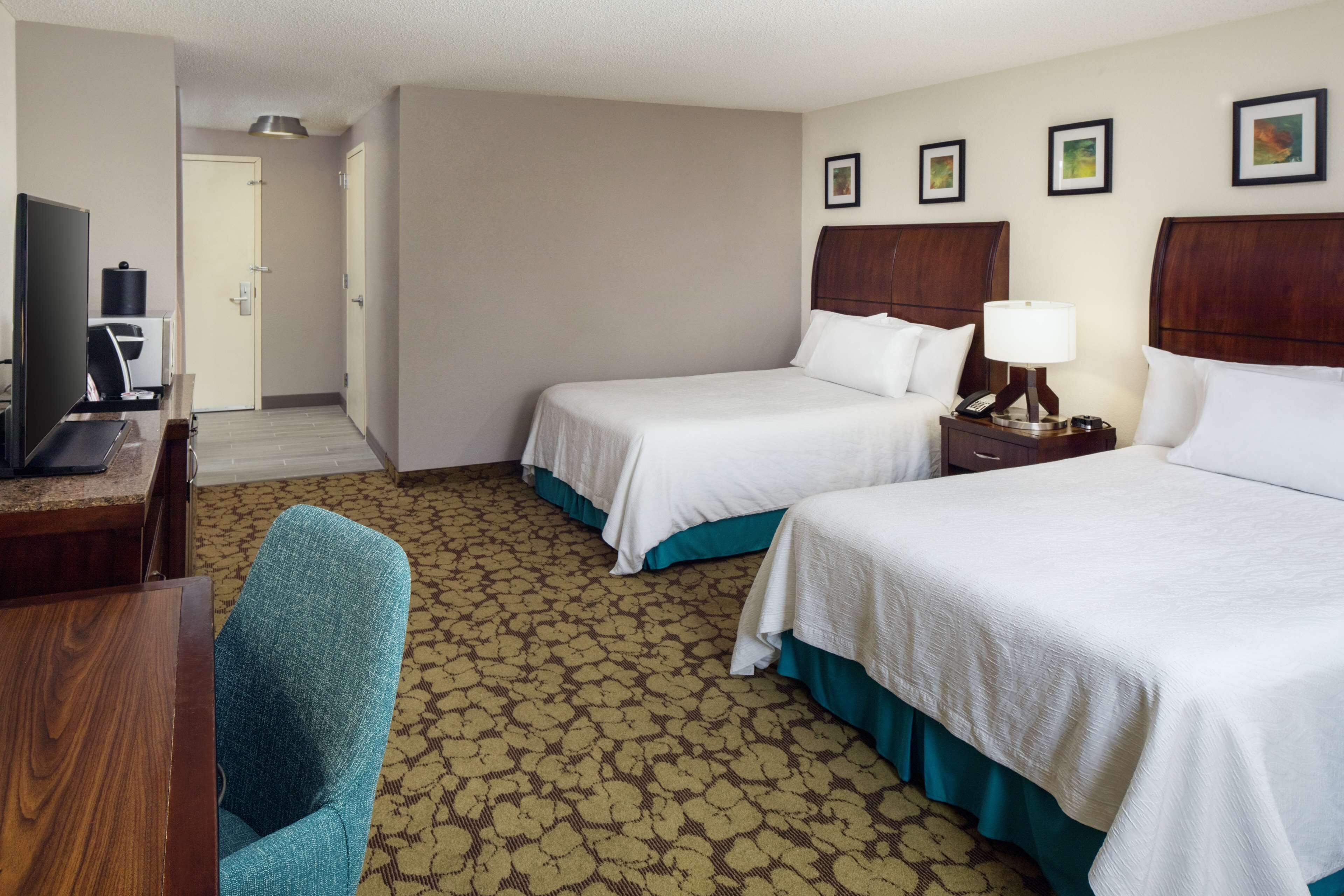 A hotel room with two beds, a desk with a computer, and a chair.