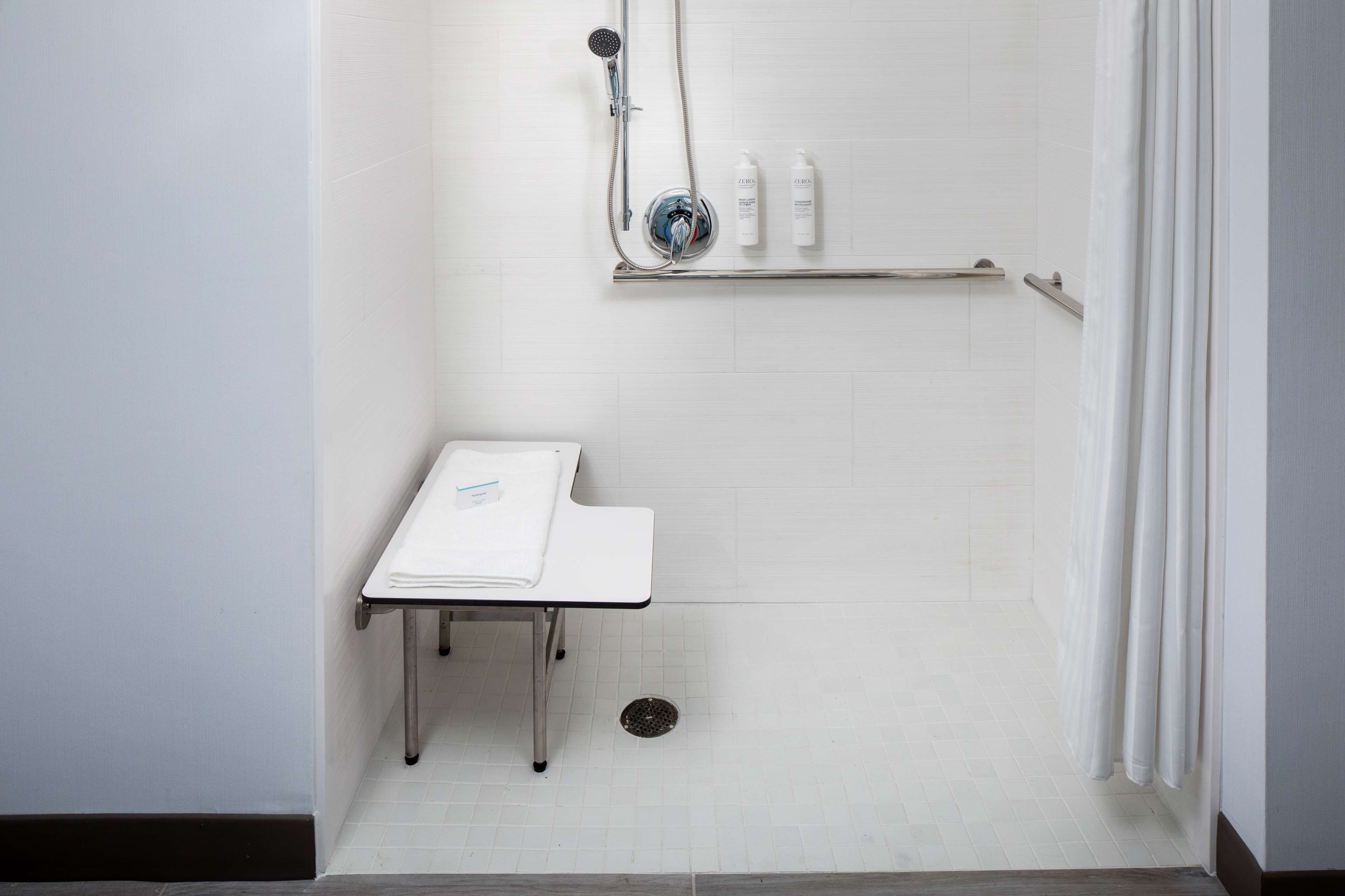 A shower area with a handheld showerhead, a shelf with toiletries, and a small table with a towel.