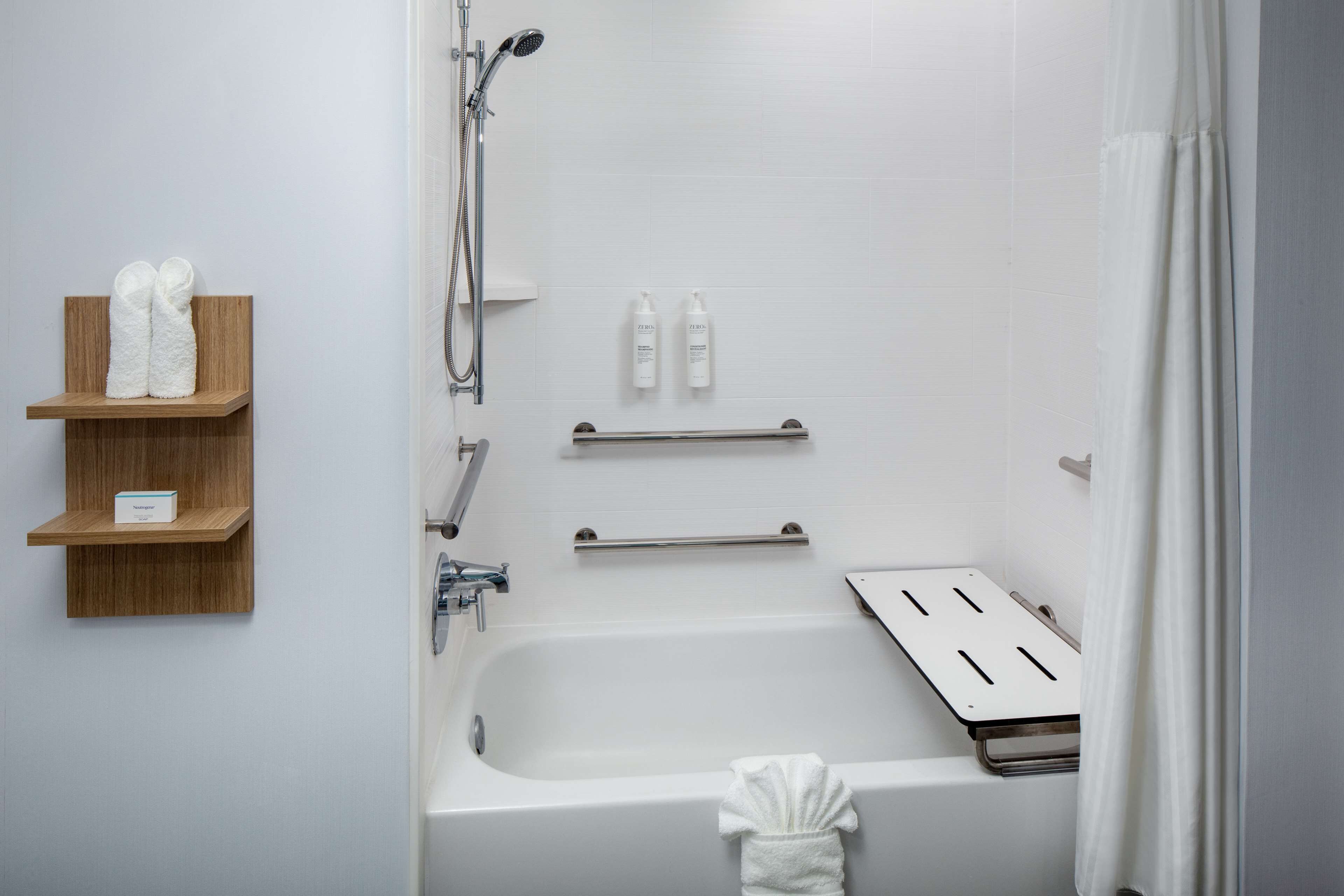 A modern bathroom with a bathtub, shower, and wooden shelves holding toiletries.