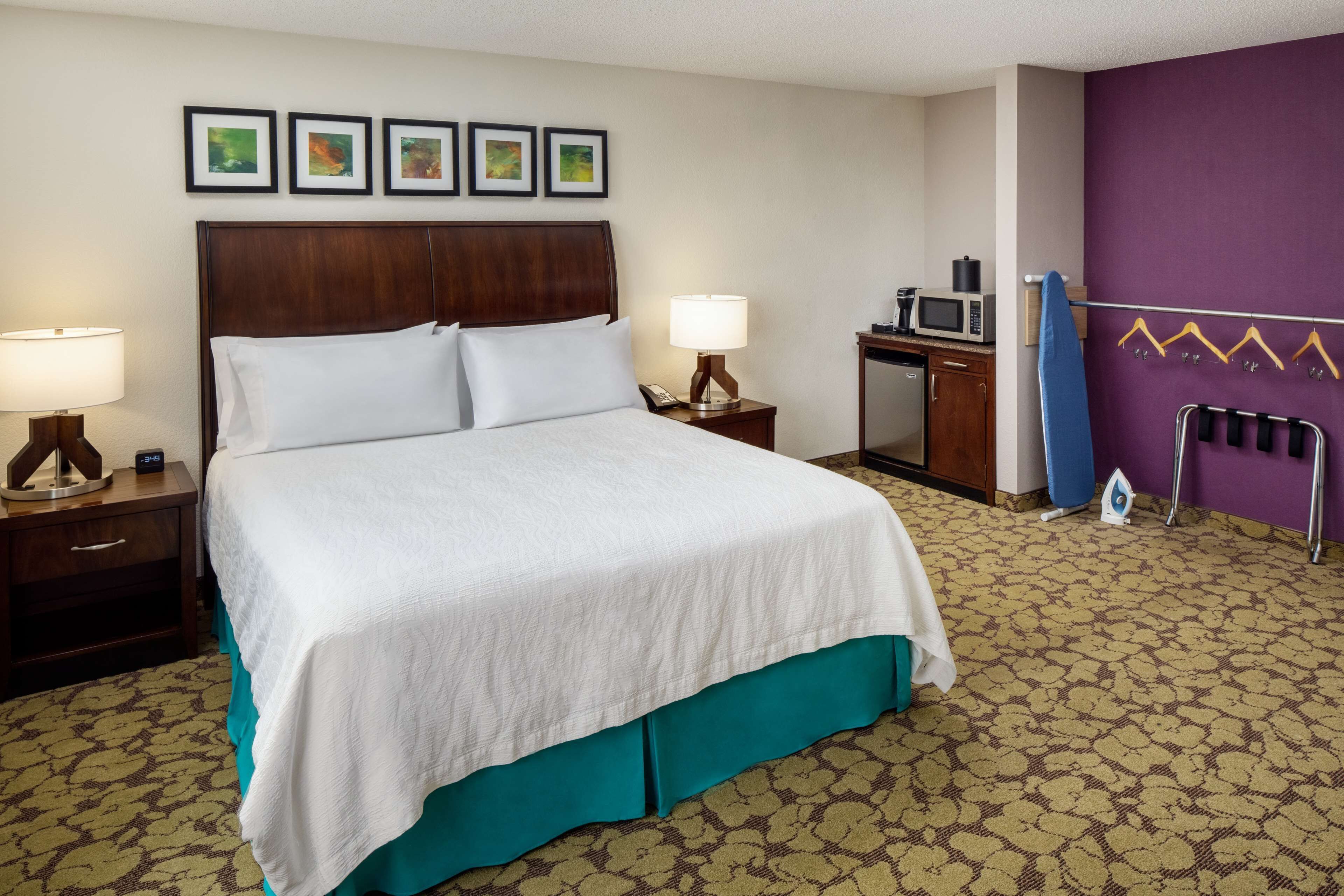 Habitación de hotel con una cama grande, dos mesitas de noche con lámparas, un aparador, un microondas y un tendedero.