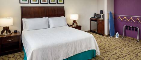 Habitación de hotel con una cama grande, dos mesitas de noche con lámparas, un aparador, un microondas y un tendedero.