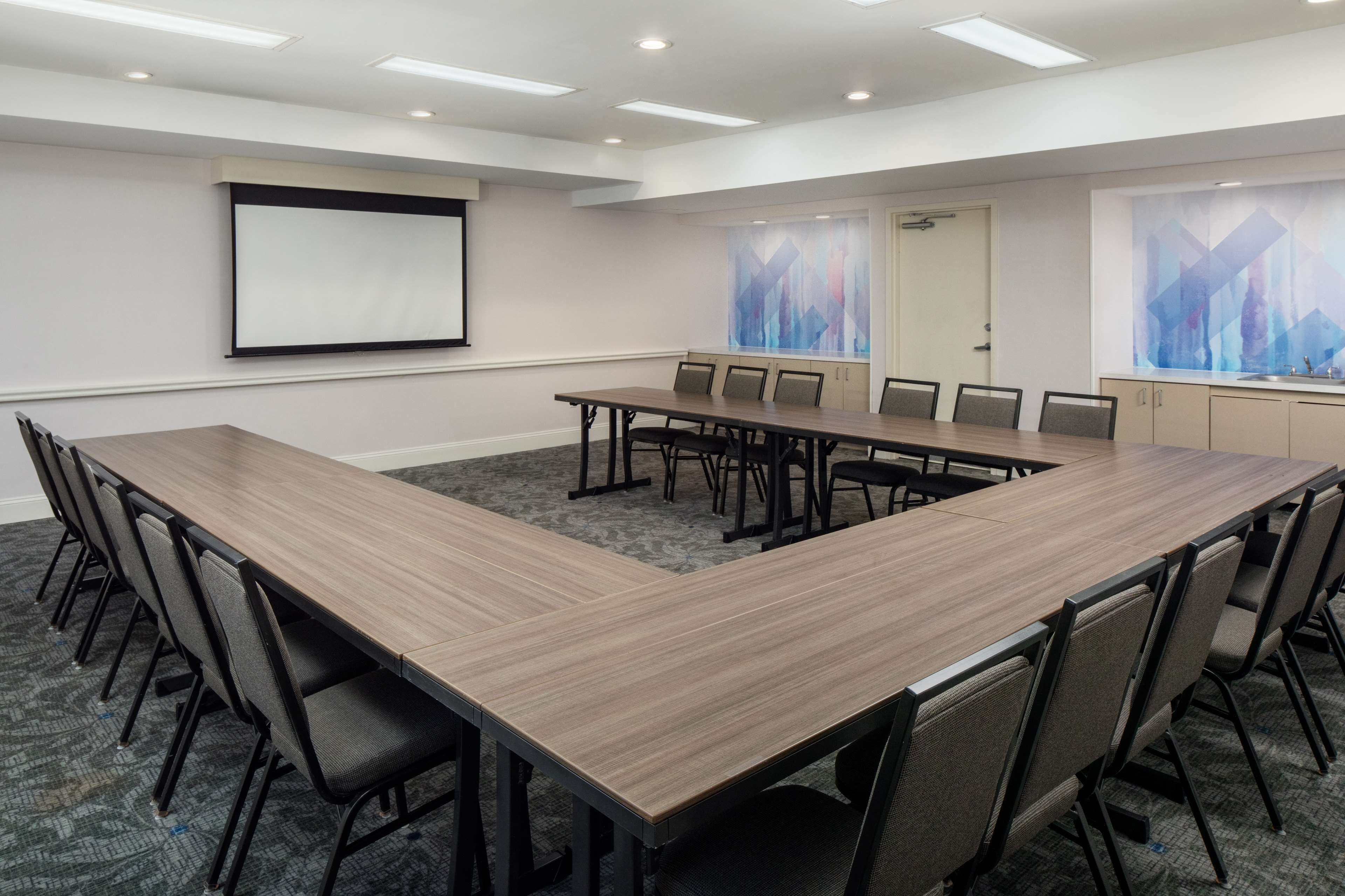 A conference room with a long table, chairs, a projector screen, and abstract wall art.