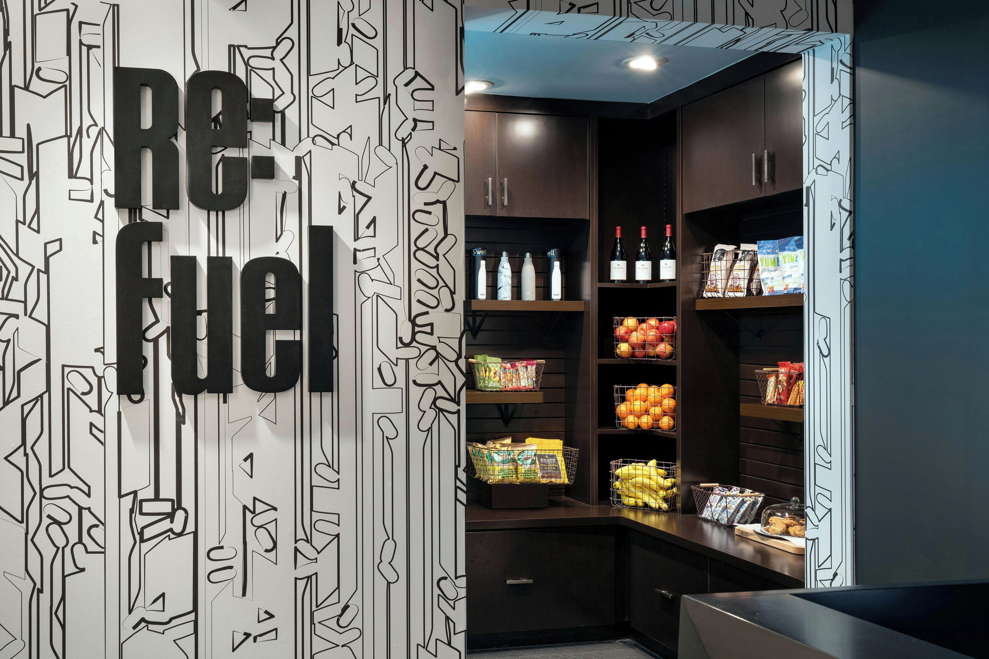 A modern kitchenette with a 'Re-fuel' sign, stocked with beverages, snacks, and fresh produce.