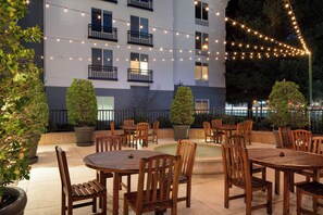 An outdoor patio area with round wooden tables and chairs, surrounded by potted plants and string lights. - Aloft by Marriott Mountain View (Mountain View)