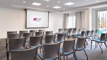 Un salón de conferencias con filas de sillas, una pantalla de proyección y un amplio ventanal.