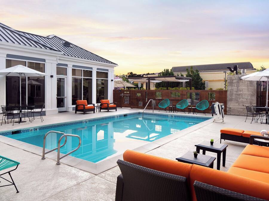 A swimming pool with lounge chairs and umbrellas, surrounded by a building with large windows.