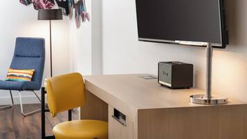 A modern room with a wooden desk, a yellow chair, a blue chair, and a flat-screen TV mounted on the wall.