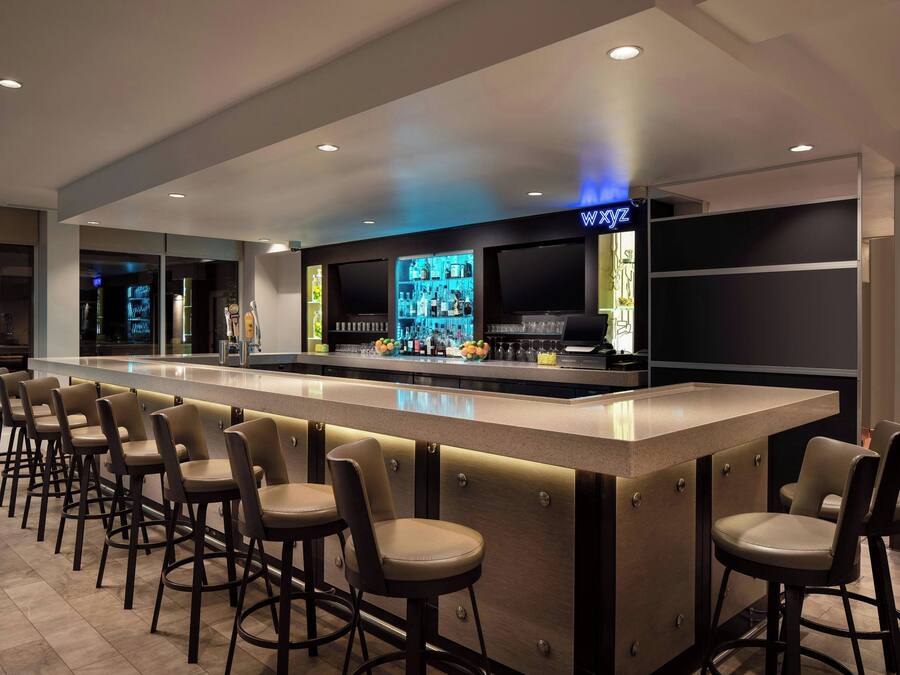 Un espace bar doté d’un long comptoir, de nombreux tabourets et d’un bar bien garni de bouteilles.