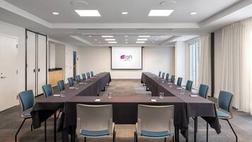 Un salón de conferencias con una larga mesa, sillas y una pantalla mostrando un logotipo.