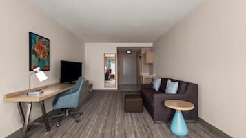 Une chambre d’hôtel équipée d’un bureau, d’une chaise, d’une télévision, d’un canapé et d’une petite table d’appoint.