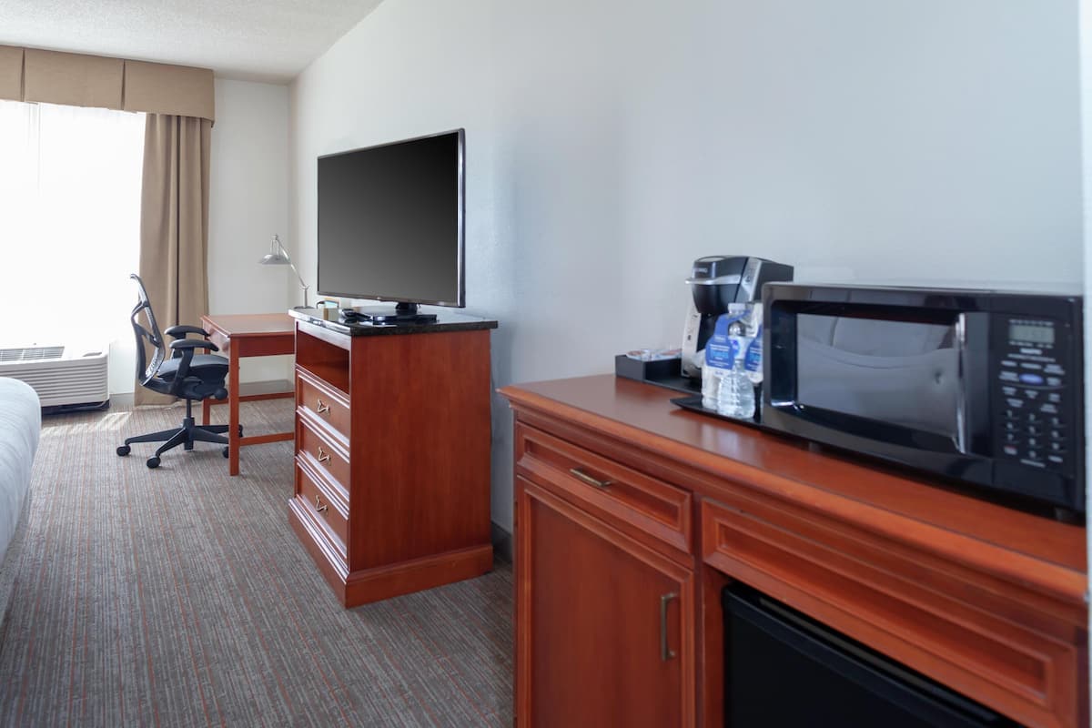 A hotel room with a bed, a desk with a chair, a television, a microwave, and a coffee maker.