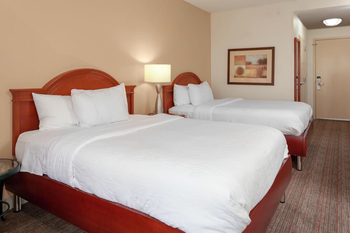 Two beds with white bedding, a lamp, a framed picture on the wall, and a door.