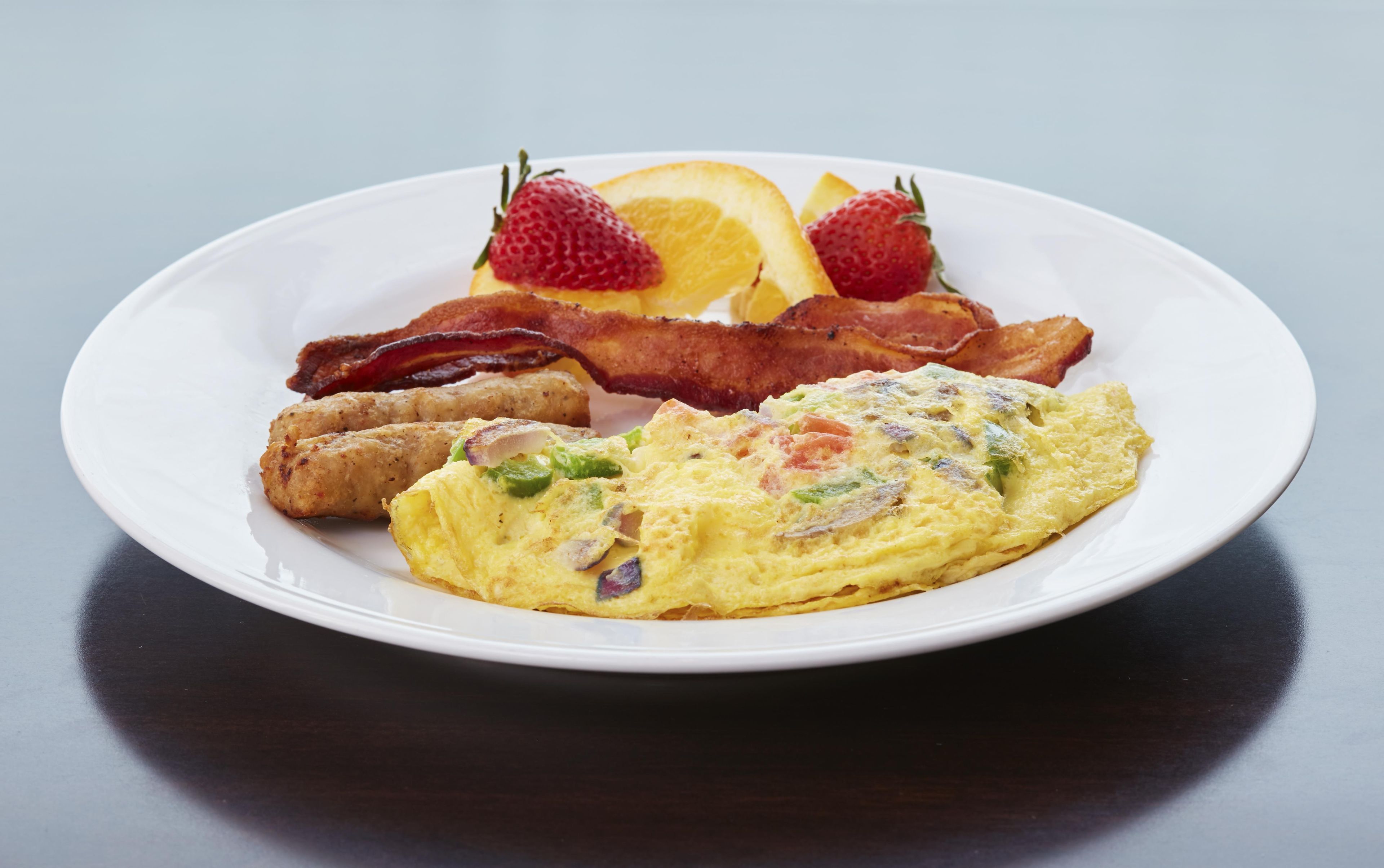 Une assiette contenant un repas de petit-déjeuner composé d’œufs, de bacon, de pain grillé et de fruits.