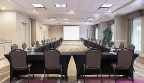 A conference room with a long table, chairs, a projector screen, and a plant. - Hilton Garden Inn Charlotte North (Charlotte)