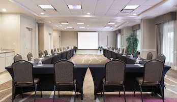 Un salón de conferencias con una larga mesa, sillas, una pantalla de proyector y una planta.