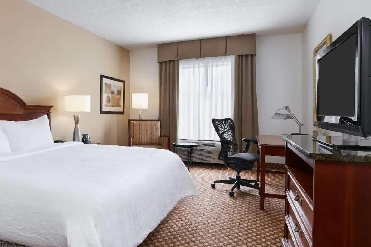 A hotel room with a large bed, a desk with a chair, a television, and a window with curtains.