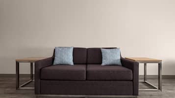 A dark brown sofa with two matching pillows against a plain wall, flanked by a wooden table on either side.