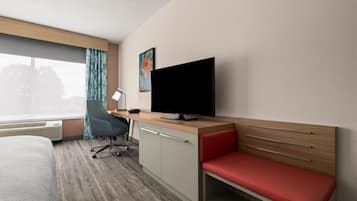 A hotel room with a bed, a desk with a computer, a TV, a chair, and a window with curtains.