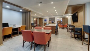 A modern dining area with multiple tables and chairs, a flat-screen TV mounted on the wall, and a kitchen area in the background. - Holiday Inn Express Nicholasville by IHG (Nicholasville)