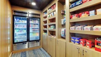 A hotel pantry with refrigerated cases and shelves stocked with snacks and beverages.