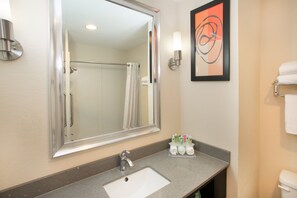 A bathroom with a large mirror, a sink, a shower, and a towel rack.