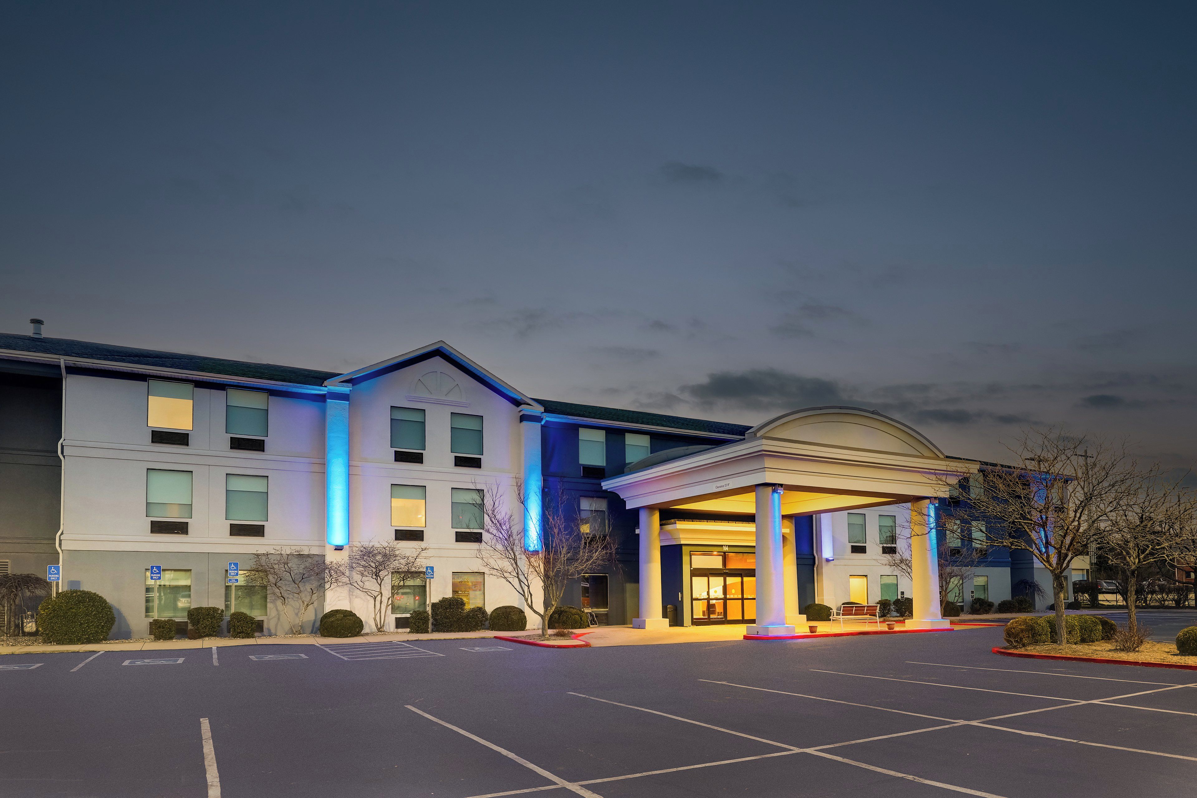 A hotel entrance with a parking lot and a building with multiple windows and a covered entrance.
