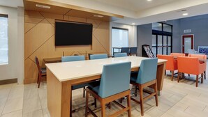 A modern conference room with a large table, blue and orange chairs, a flat-screen TV, and a projection screen. - Holiday Inn Express Nicholasville by IHG (Nicholasville)