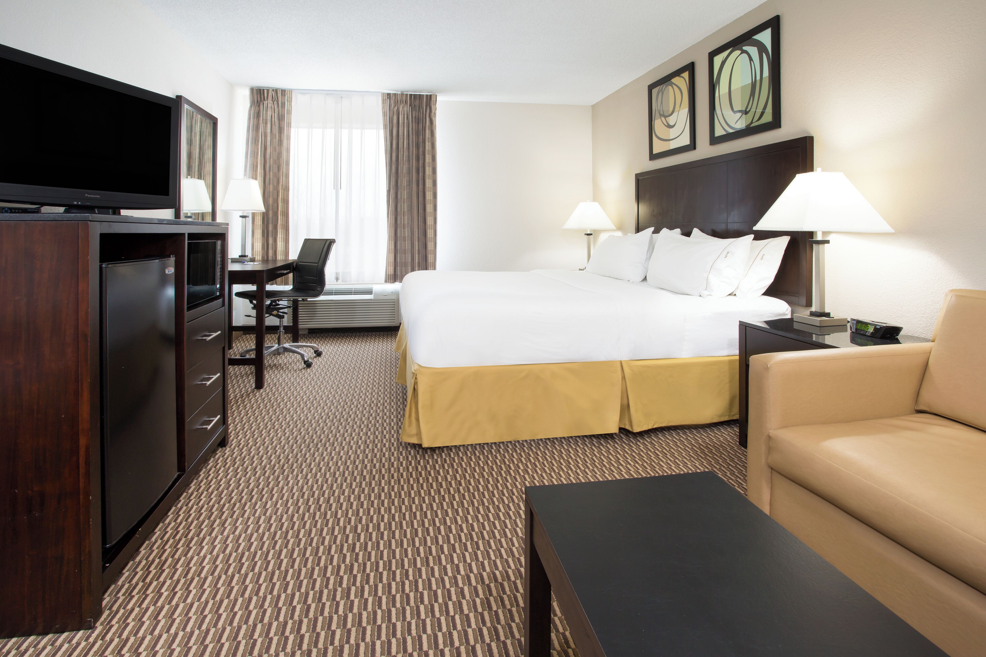 A hotel room with a bed, a TV, a desk, a chair, and a sofa.