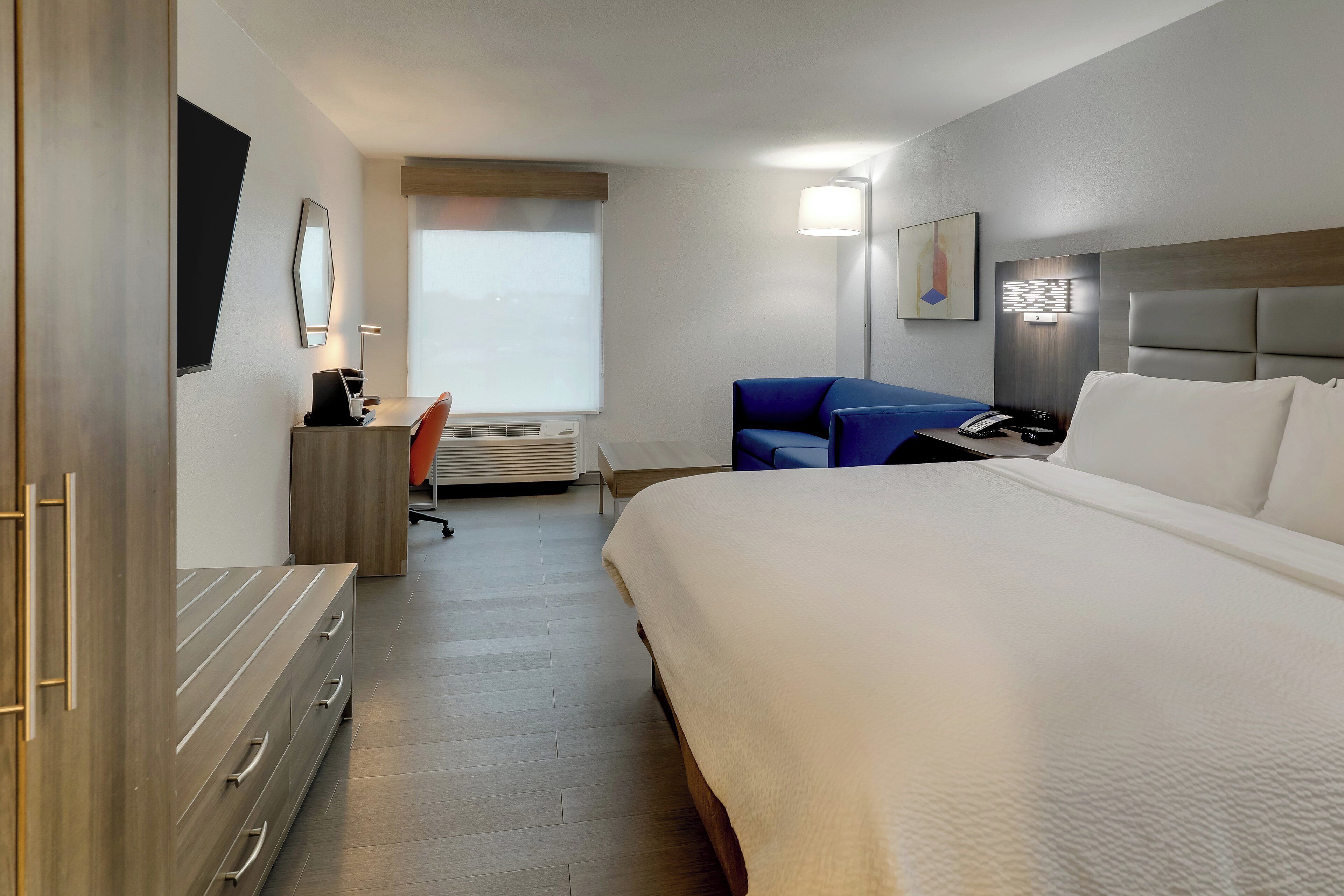 A hotel room with a large bed, a desk with a computer, a chair, and a lamp.