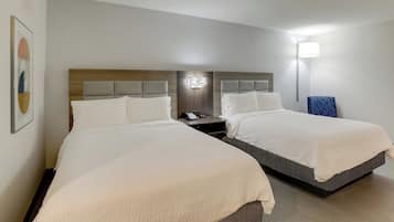 Habitación de hotel con dos camas, una mesita de noche, una lámpara de pared y un cuadro enmarcado.