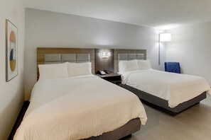 A hotel room with two beds, a nightstand, a wall-mounted lamp, and a framed picture.