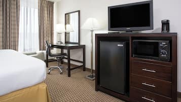 A hotel room with a bed, desk, chair, lamp, television, refrigerator, and microwave.