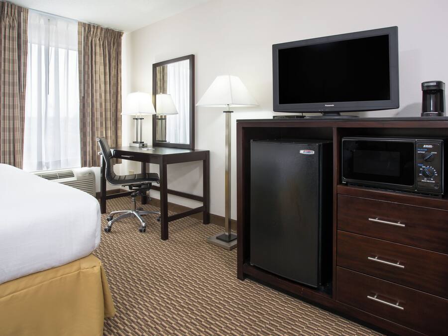 A hotel room with a bed, desk, chair, lamp, television, refrigerator, and microwave.