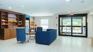 A lobby with a reception desk, blue seating, and a large glass door leading outside. - Clarion Pointe-Dillard near Blue Ridge Mountains (Dillard)