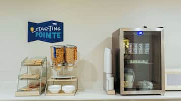Una barra de desayuno con máquina de café, dispensadores de cereal y un refrigerador.