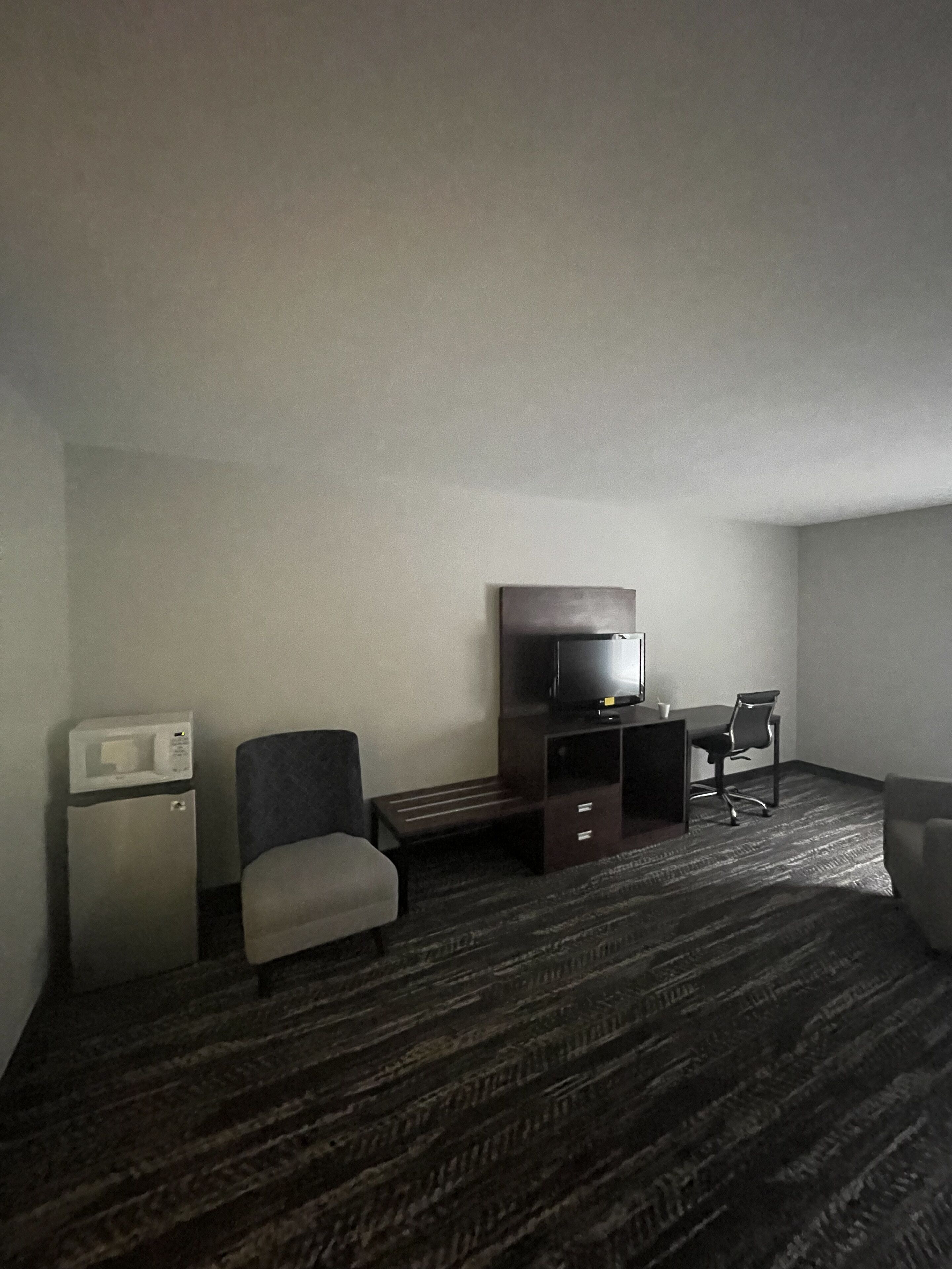 A hotel room with a bed, a desk with a chair, a television, and a microwave.