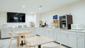 A modern kitchen with white cabinets, a flat-screen TV, a microwave, and a coffee machine. - Clarion Pointe-Dillard near Blue Ridge Mountains (Dillard)