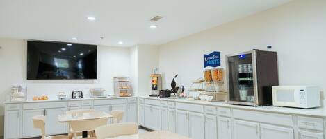 A modern kitchen with white cabinets, a flat-screen TV, a microwave, and a coffee machine.