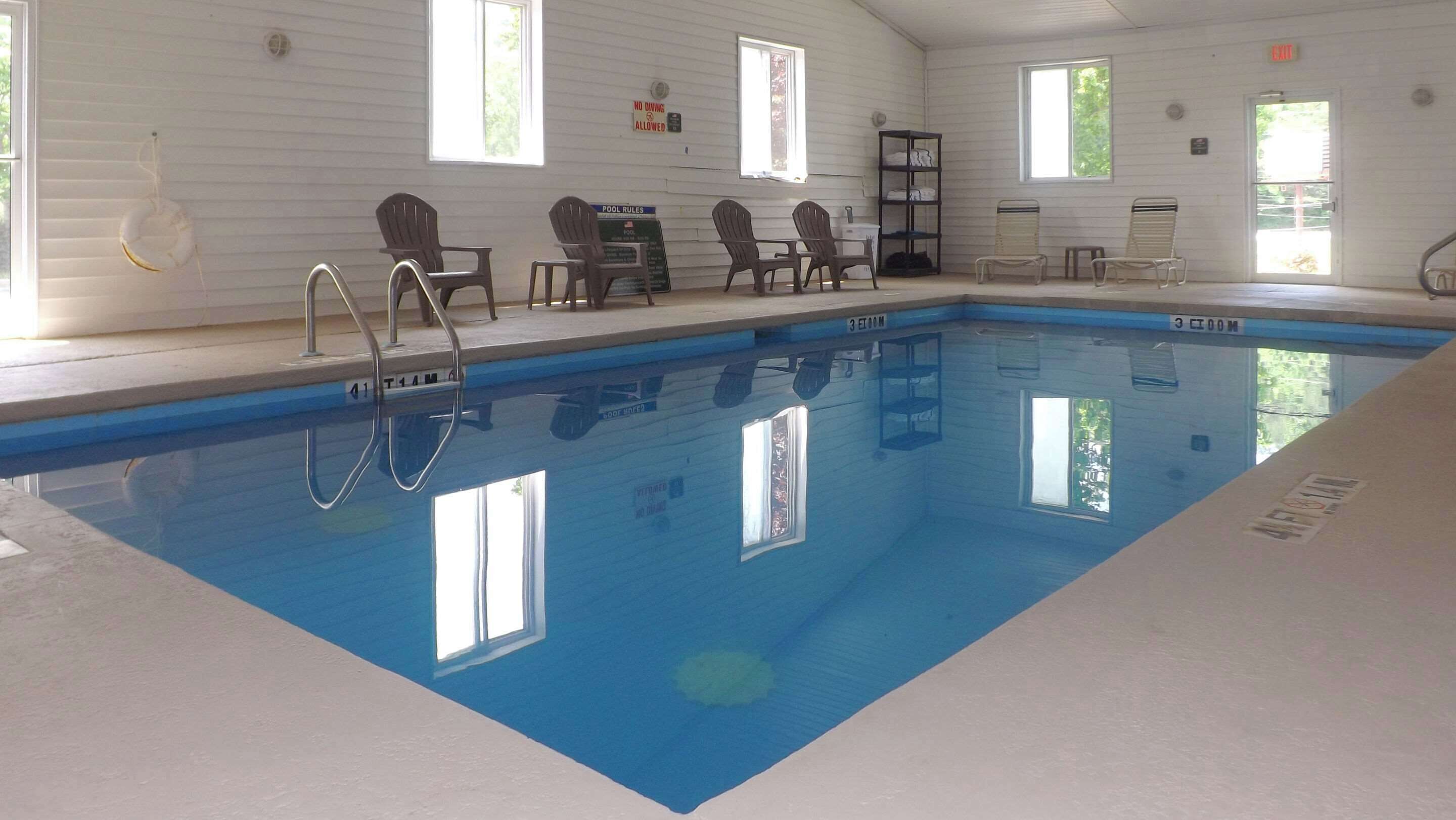 Una piscina interior con señalización clara de las normas, chalecos salvavidas y sillas alrededor del área de la piscina.