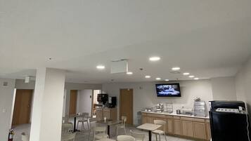 A spacious indoor area with multiple seating arrangements, a kitchen area, and a television mounted on the wall.