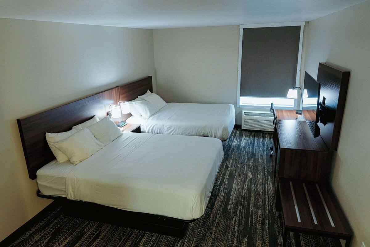 A hotel room with two beds, a desk with a chair, a TV, and a window with blinds.