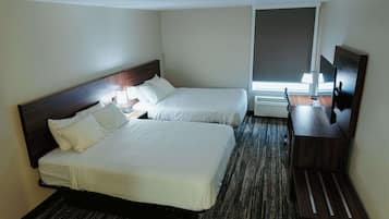 A hotel room with two beds, a desk with a chair, a TV, and a window with blinds.
