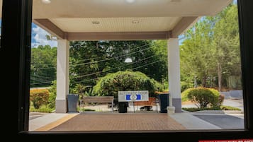 Una entrada con puerta automática, un banco y un cartel que indica empujar en caso de emergencia.