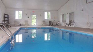 An indoor swimming pool with clear blue water, surrounded by lounge chairs and a white interior. - Clarion Pointe-Dillard near Blue Ridge Mountains (Dillard)