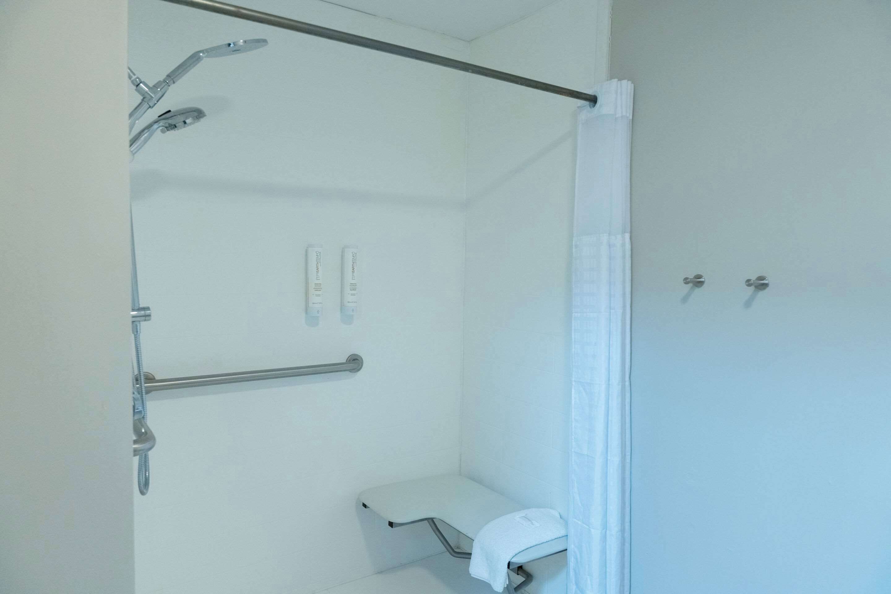 A bathroom with a shower, grab bars, a toilet, and a towel rack.