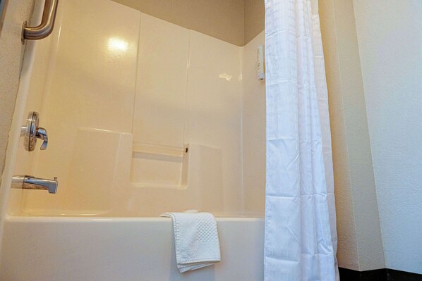 A white bathtub with a shower curtain, a towel, and a handrail.