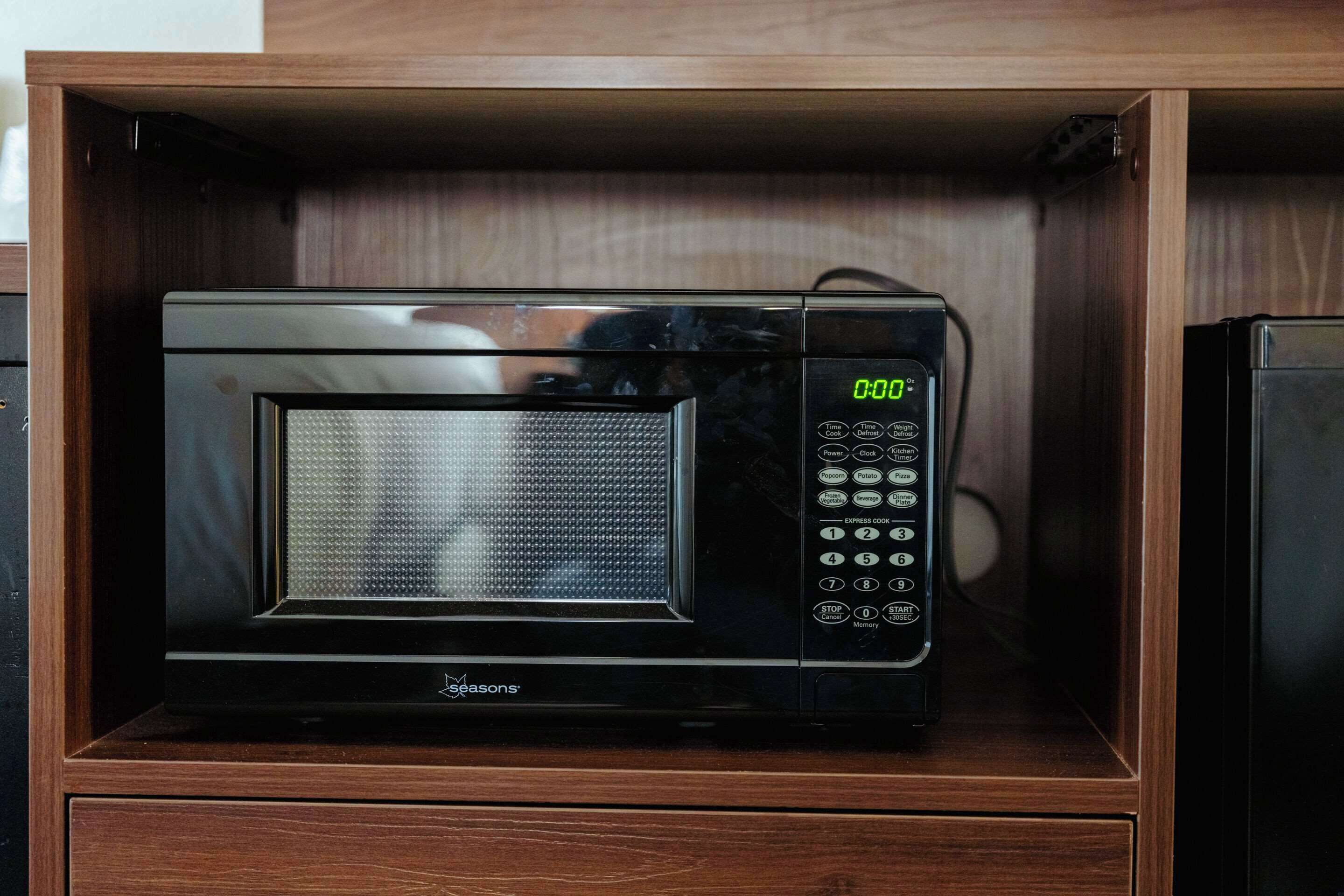 A black microwave in a wooden cabinet with a digital display and control buttons.