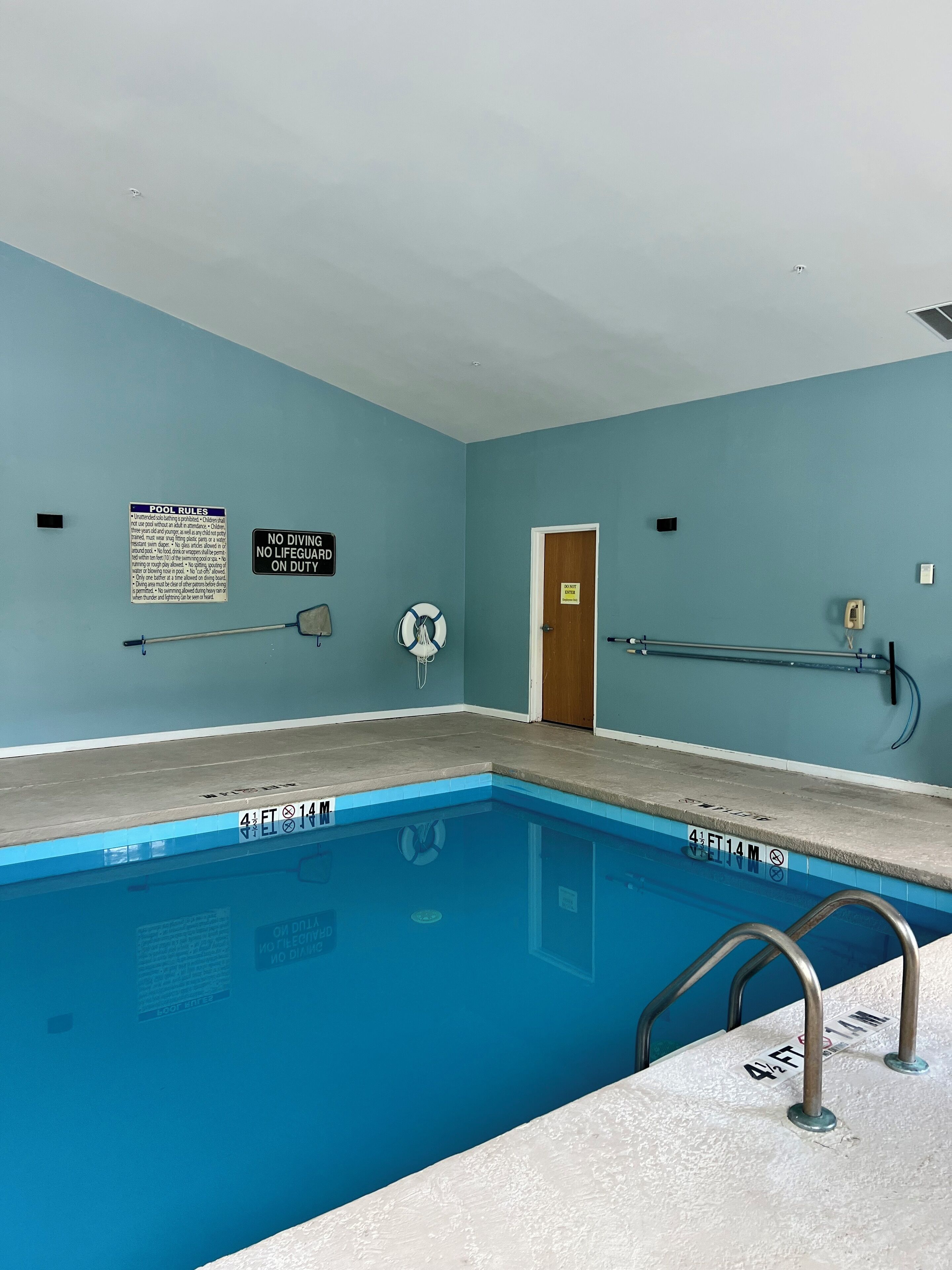 A swimming pool with clear water, marked depth, and safety signs.