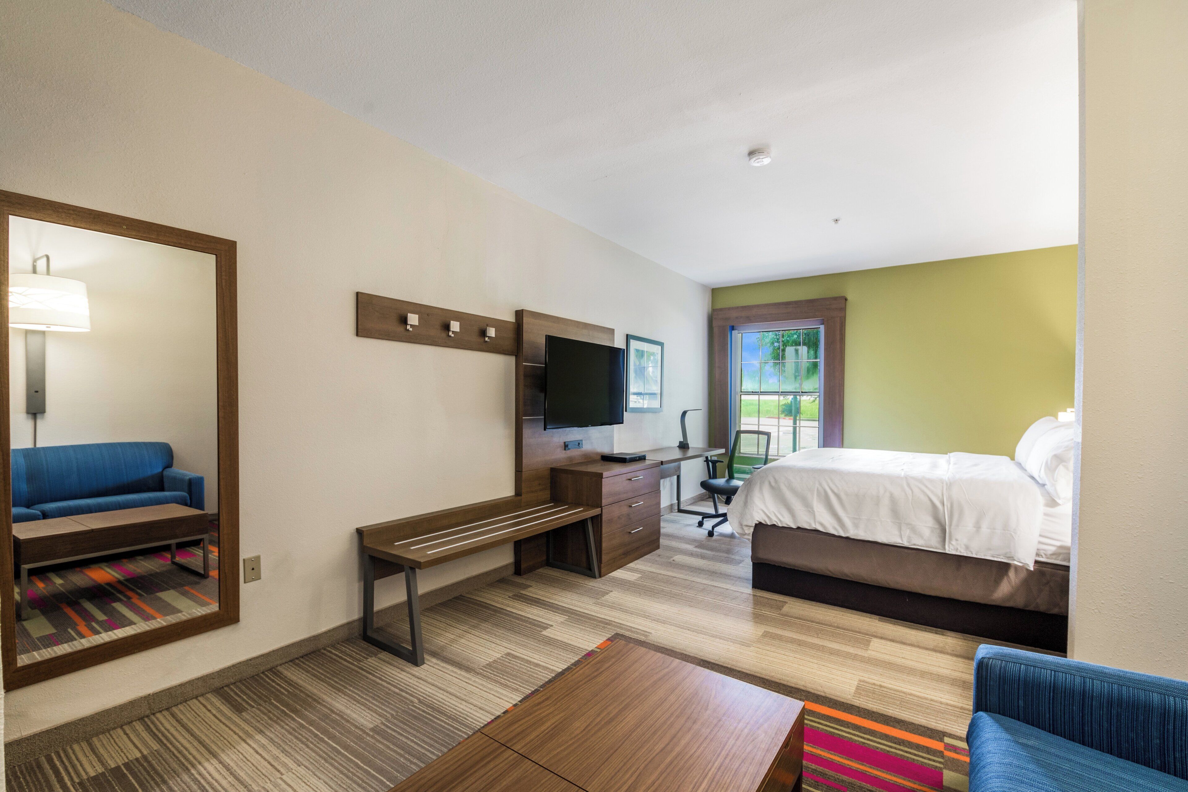 Habitación de hotel con cama, escritorio, silla, sofá, televisión y ventana.